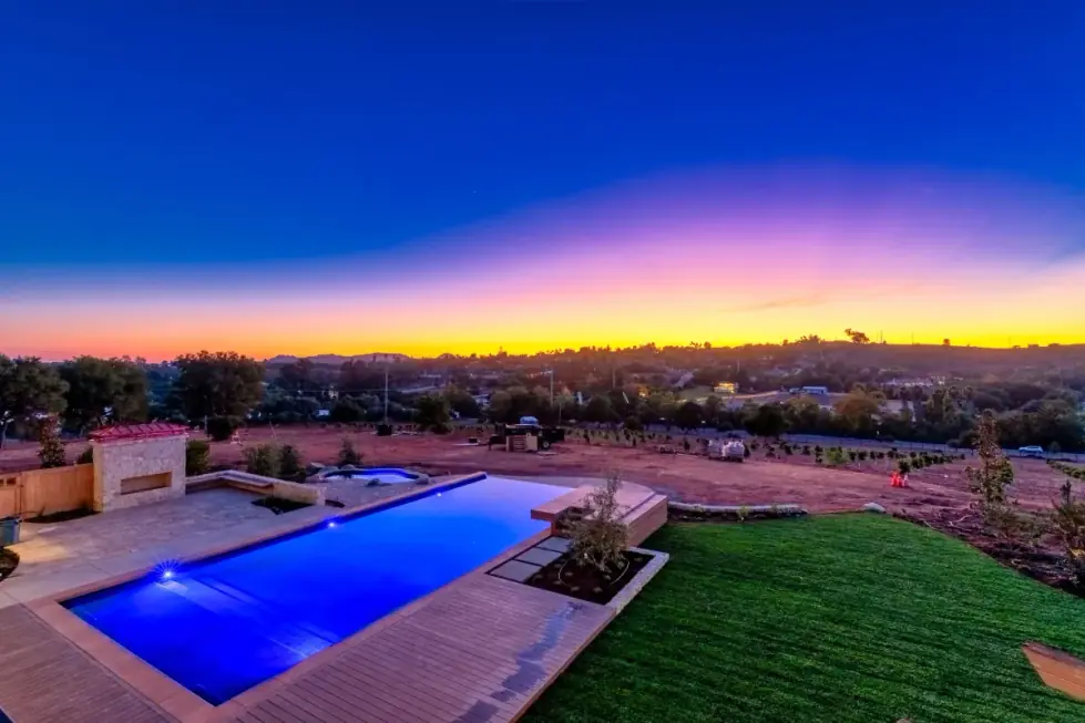 A backyard pool photographed at blue hour with a vivid sunset sky